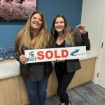 Two people holding a sold home sign